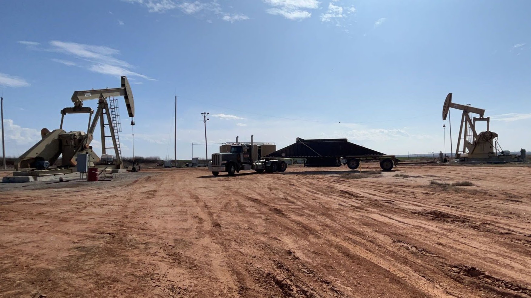 Gorilla Construction semi with a belly dump trailer on a red dirt oil lease between pump jacks
