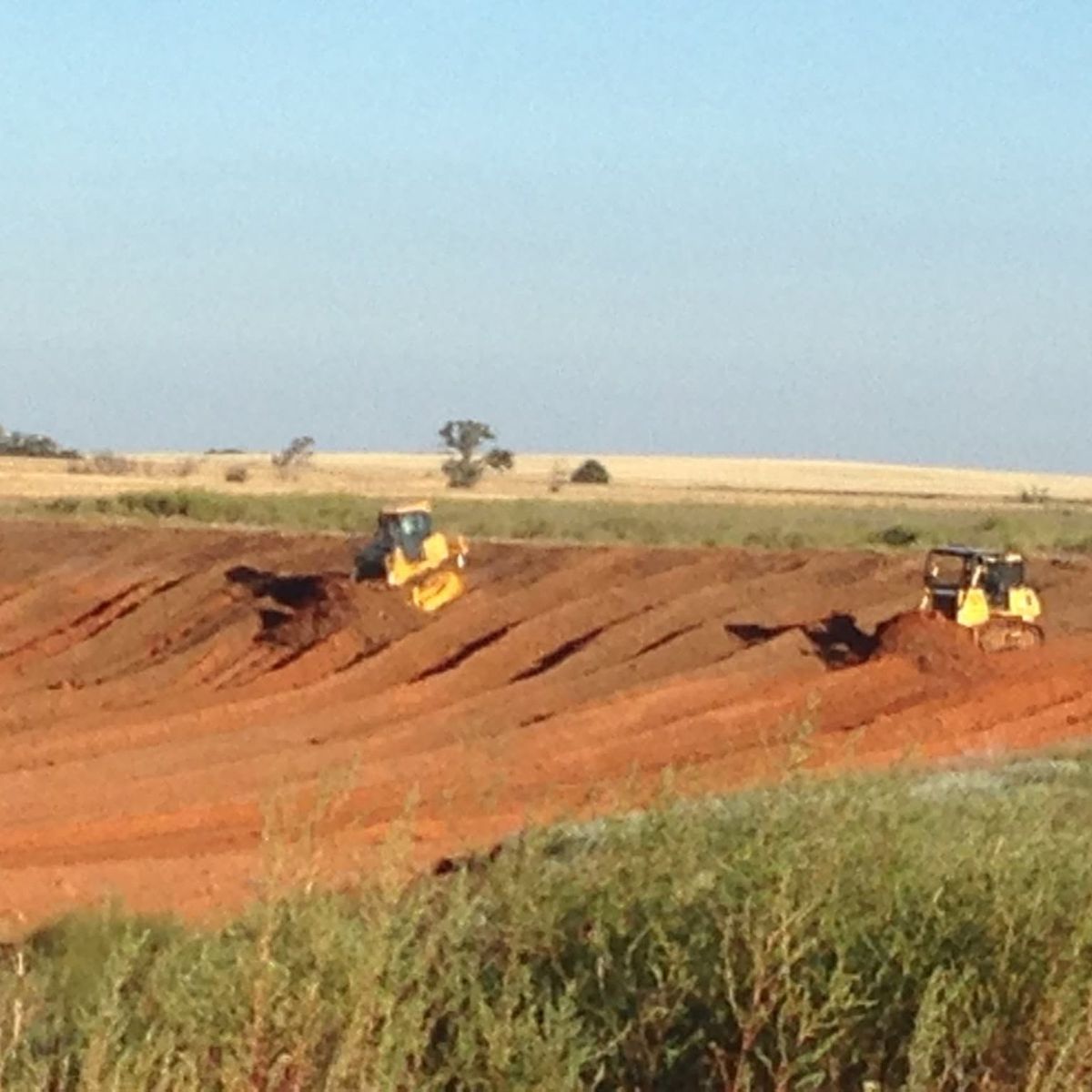 Two yellow dozers working a cut of red dirt on open prairie