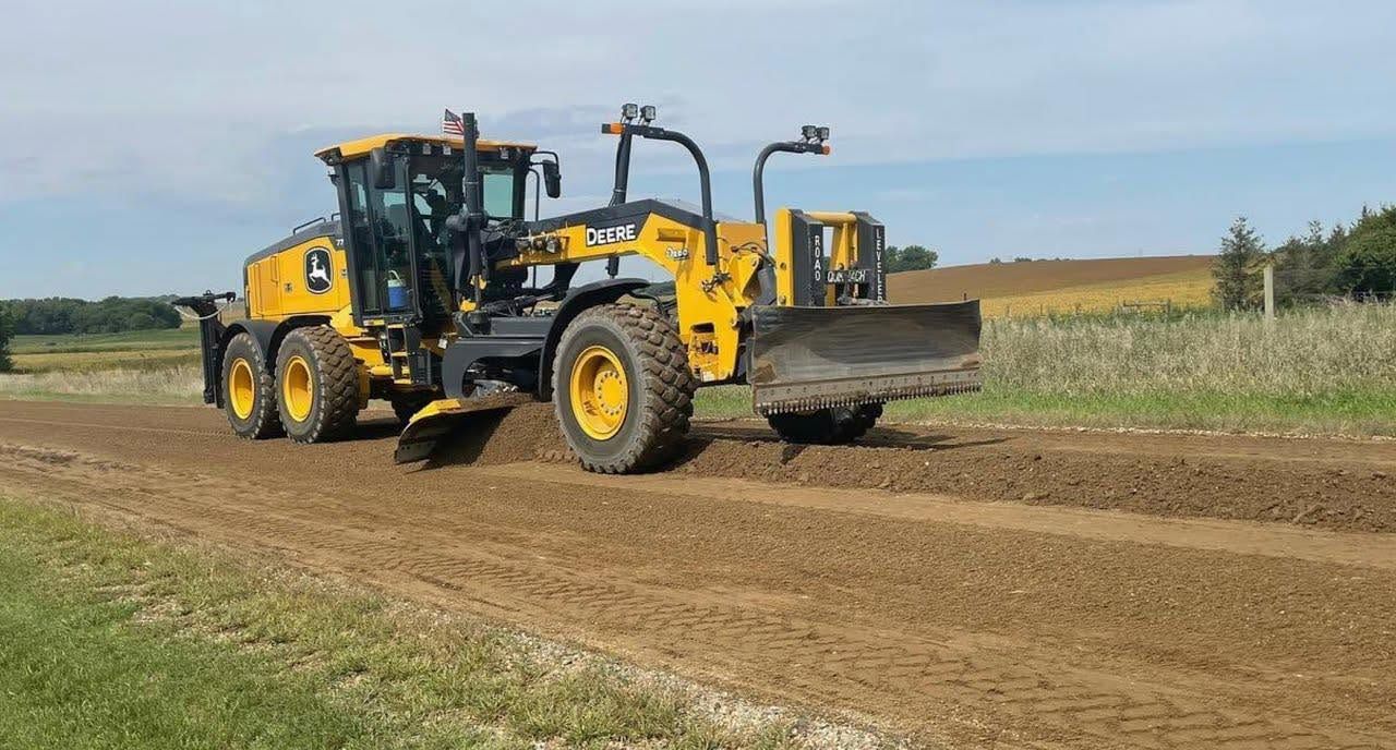 Yellow John Deere motor grader smoothing a dirt road